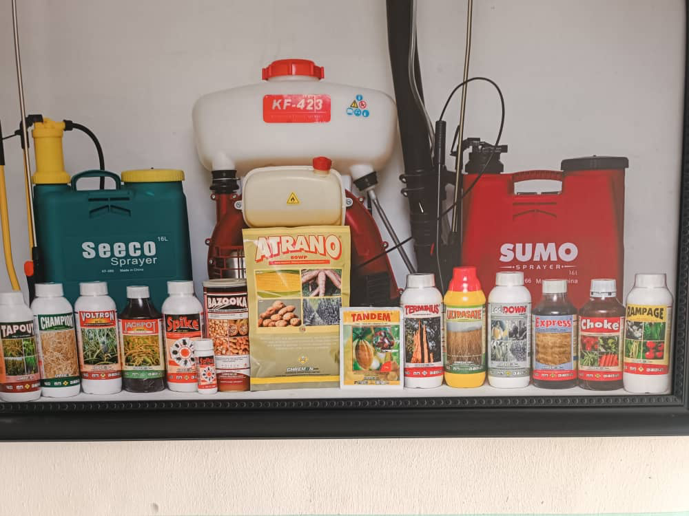 A shelf of Chremon crop protection bottles, packets, and backpack sprayers